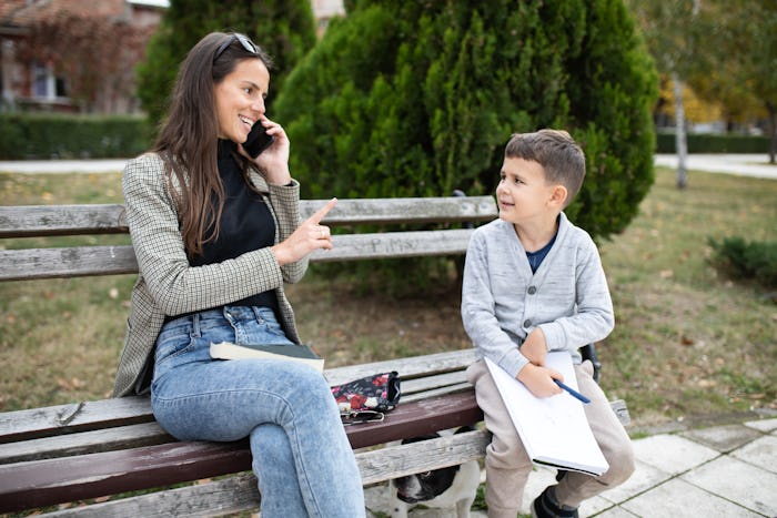 A young mom is talking on the phone and raising her index finger at her son who is interrupting her ...