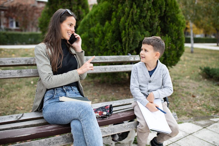 A young mom is talking on the phone and raising her index finger at her son who is interrupting her ...