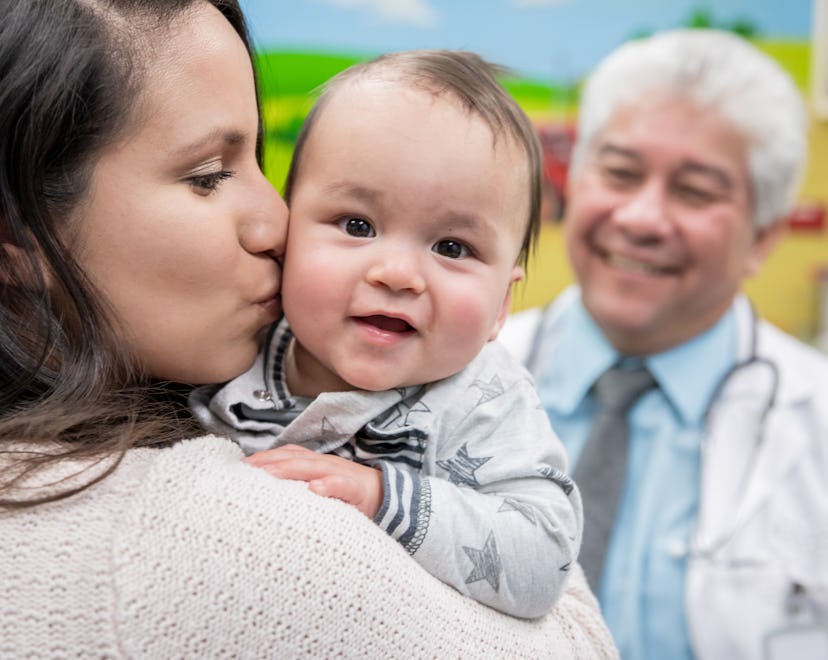 Baby smiling while looking over moms shoulder in pediatrician office, considering tongue tie release...