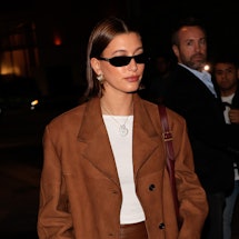 Hailey Bieber wears a brown leather duster coat, a leather skirt, and white tee