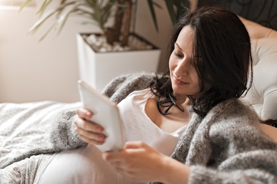 Pregnant woman rests in bed while reading her tablet, in a story about the dirtiest books on Kindle.