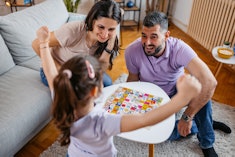 Young mother and father playing a Ludo board game with their daughter in the living room. Daughter w...