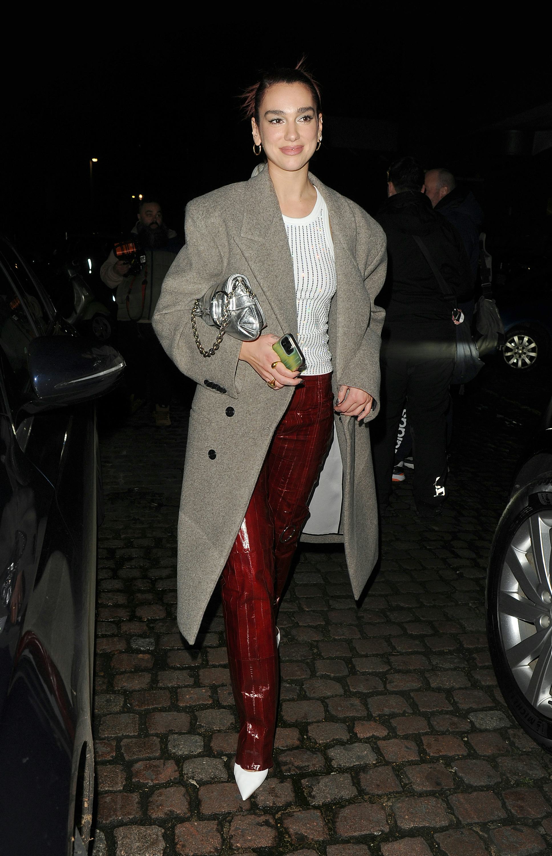 Dua Lipa wears a white tank, burgundy pants, white pumps, and the latest Gucci Horsebit Chain bag.