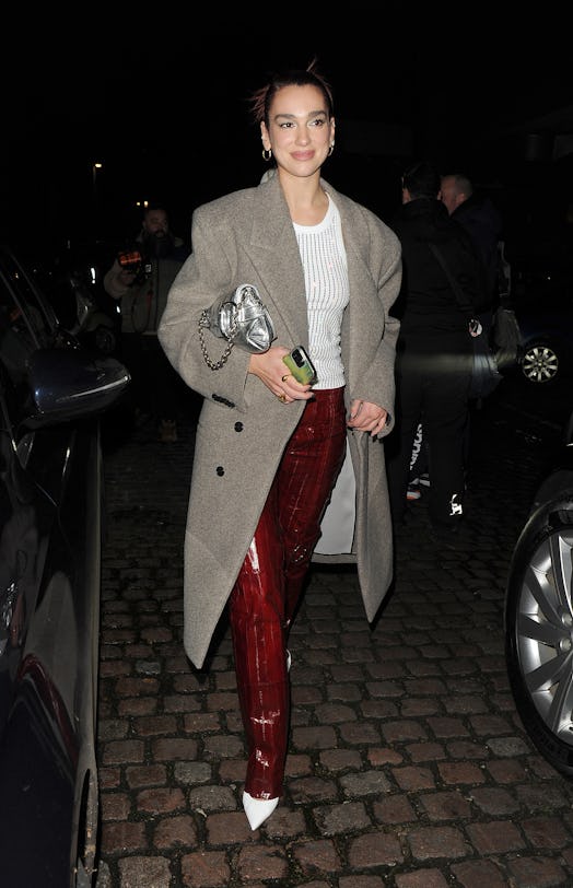 Dua Lipa wears a white tank, burgundy pants, white pumps, and the latest Gucci Horsebit Chain bag.