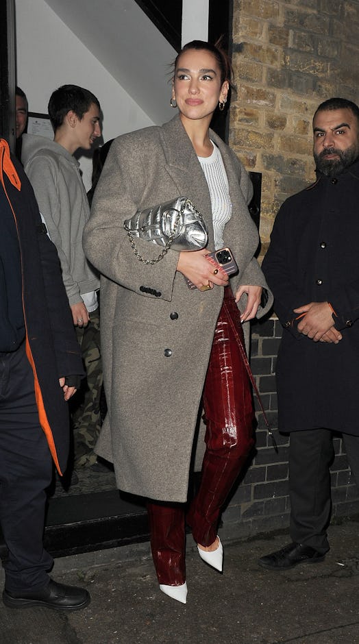 Dua Lipa wears a white tank, burgundy pants, white pumps, and the latest Gucci Horsebit Chain bag.
