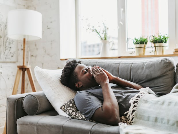 Young adult black man lying down at home with a flu and runny nose