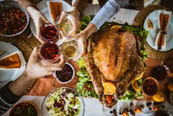 Above view of unrecognizable extended family toasting during Thanksgiving meal at dining table.