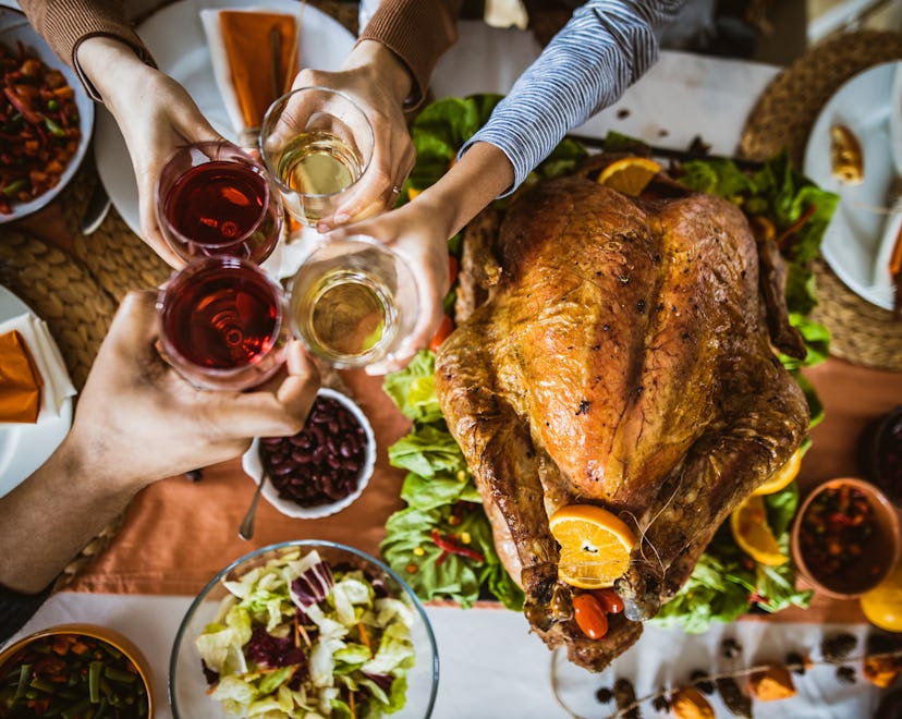 Above view of unrecognizable extended family toasting during Thanksgiving meal at dining table.