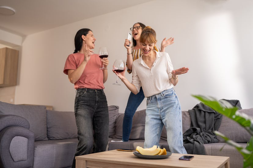 Female friends having fun singing and dancing living room at home.