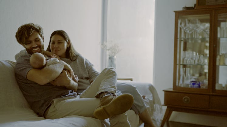 Mother, father and baby on a sofa as a family in the living room of their home together for love, ca...