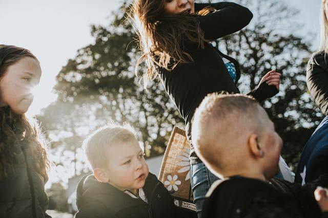 A family / group of children and adults get prepared to go on an outdoors excursion. The scene is bu...