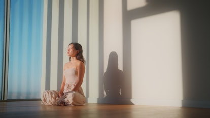 A young woman is meditating in a domestic room under sunlight.
