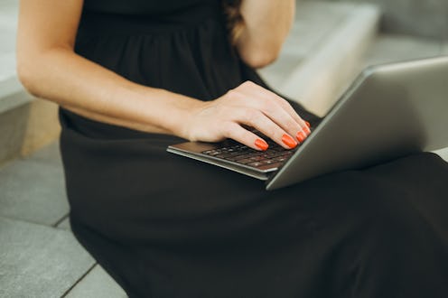 Close up shot of cropped young woman in black dress using ultrabook while sitting on gray steps.