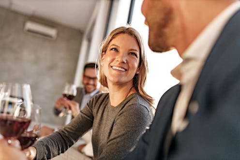 Happy female entrepreneur communicating with her colleague while toasting with red wine in the offic...