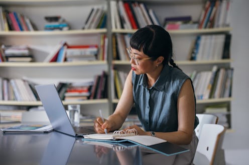 A serious Japanese entrepreneur taking notes while reading something on her laptop. She is sitting a...