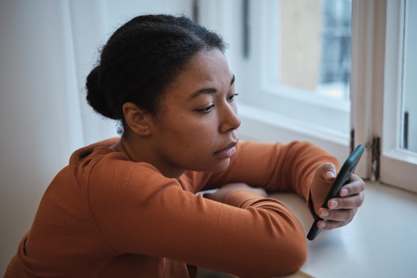 Sad worried African American woman using smartphone at home, scrolling social media  feeling depress...