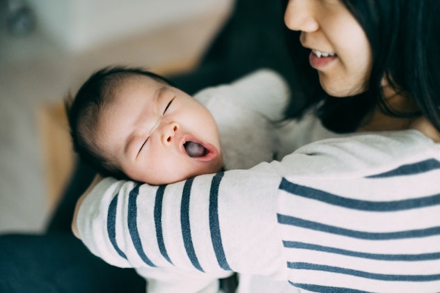 Caring Asian young mother holding yawning baby in arms with love and smile