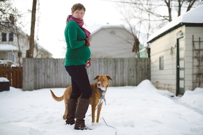 27 weeks pregnant, short haired woman in green stands in snow with dog, in a story answering the que...