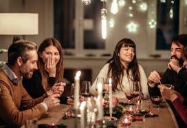 Friends enjoying Christmas dinner party at home, in a story about questions to ask at social gatheri...