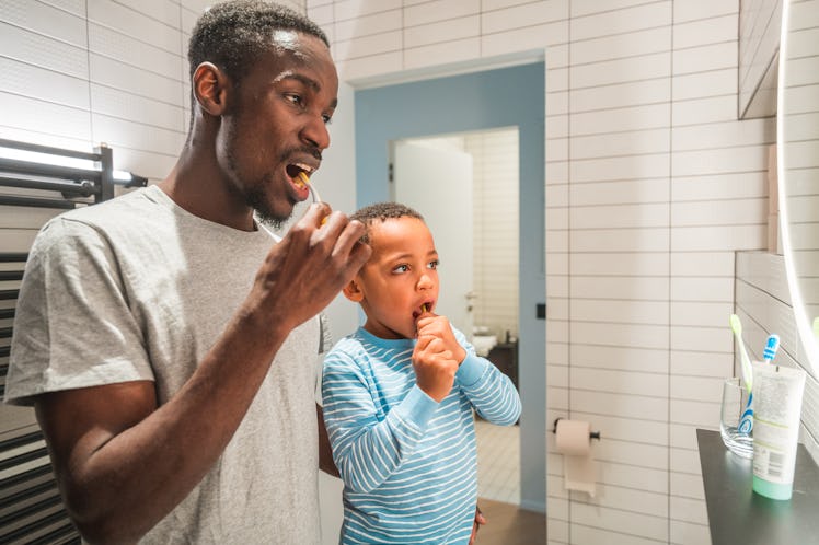 Mid adult Black male and his cute boy doing their night routine together. They are standing in a bat...