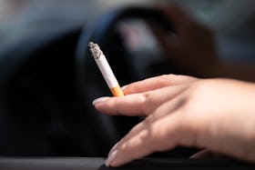 PRODUCTION - 15 August 2023, Saxony, Dresden: A woman sits in a car and holds a cigarette. According...