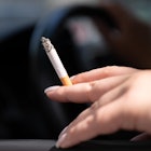 PRODUCTION - 15 August 2023, Saxony, Dresden: A woman sits in a car and holds a cigarette. According...