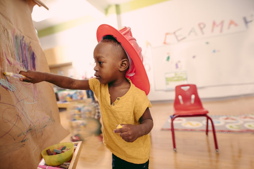 A preschooler drawing on an easel in class.