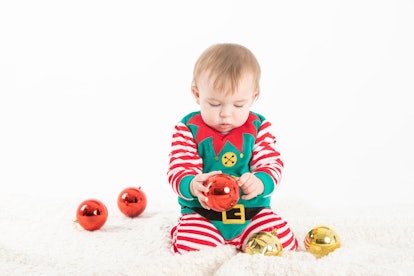 Stock studio photo with white background of a baby in elf costume grabbing christmas balls with seri...