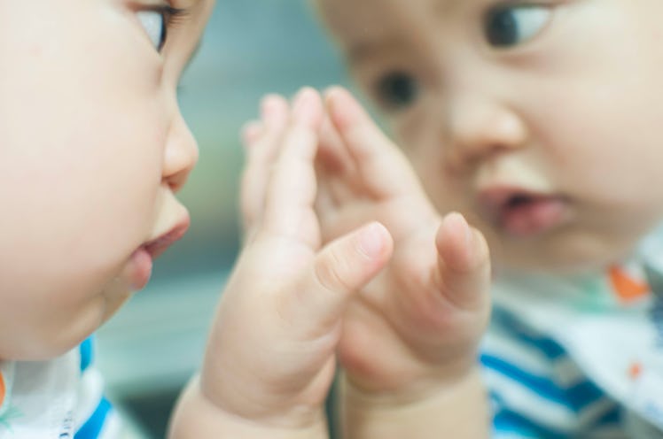 A baby boy is looking at his reflection in the mirror.