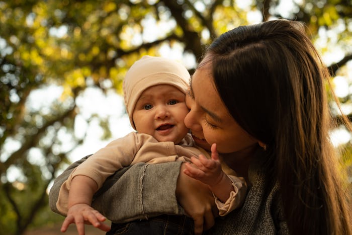 Woman kissing baby in park in autumn.