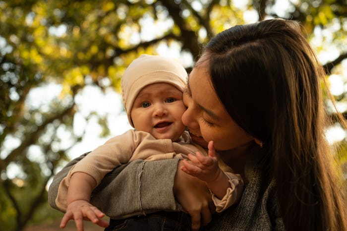 Woman kissing baby in park in autumn.