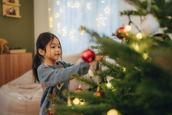 Little girl decorating Christmas tree at home, in a story about the history of the Christmas tree.