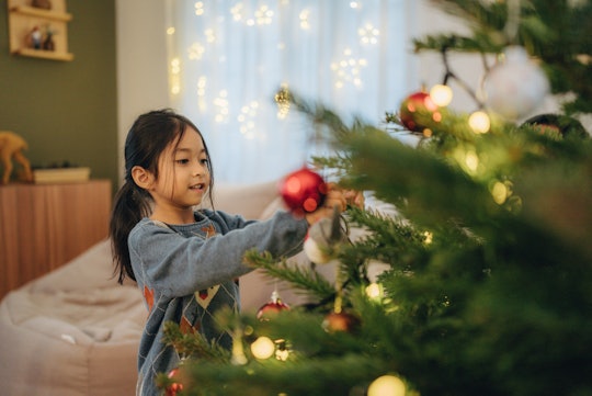 Little girl decorating Christmas tree at home, in a story about the history of the Christmas tree.