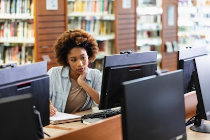 A young African-American woman in her 20s using a desktop computer in the library.