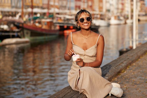 Happy young woman with ice cream cup wearing sunglasses while sitting on promenade