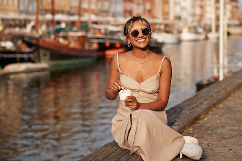 Happy young woman with ice cream cup wearing sunglasses while sitting on promenade