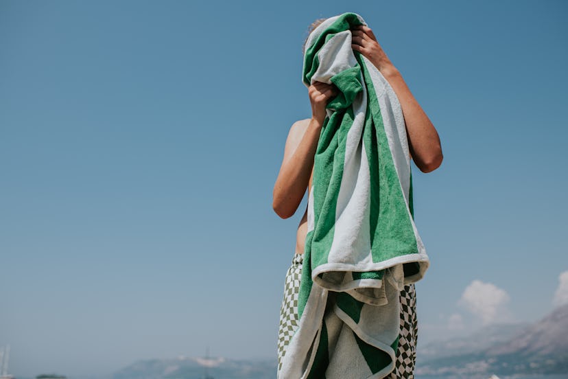 A lad uses a large green and white striped beach towel to dry his face and hair after swimming in th...