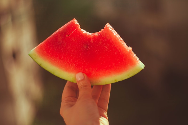 A woman’s hand holding a slice of bitten watermelon