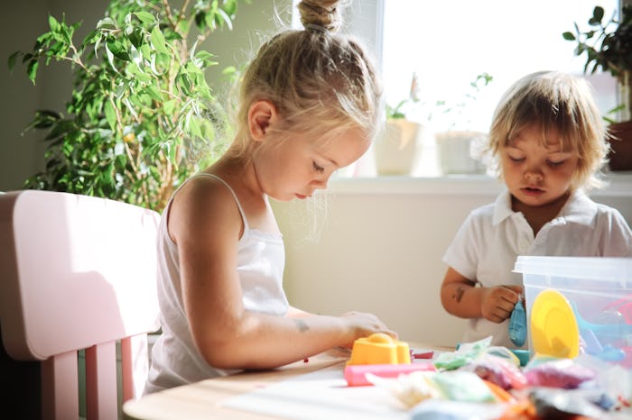 Sister and brother, sibling children molding from modeling clay together at the table. Sibling relat...