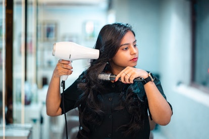 Portrait of Female hairdresser at the salon holding styling her hair using hair dryer and Round Hair...