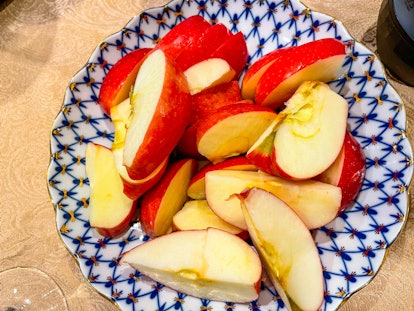 Sliced red apples in decorative crockery bowl atop gold tablecloth