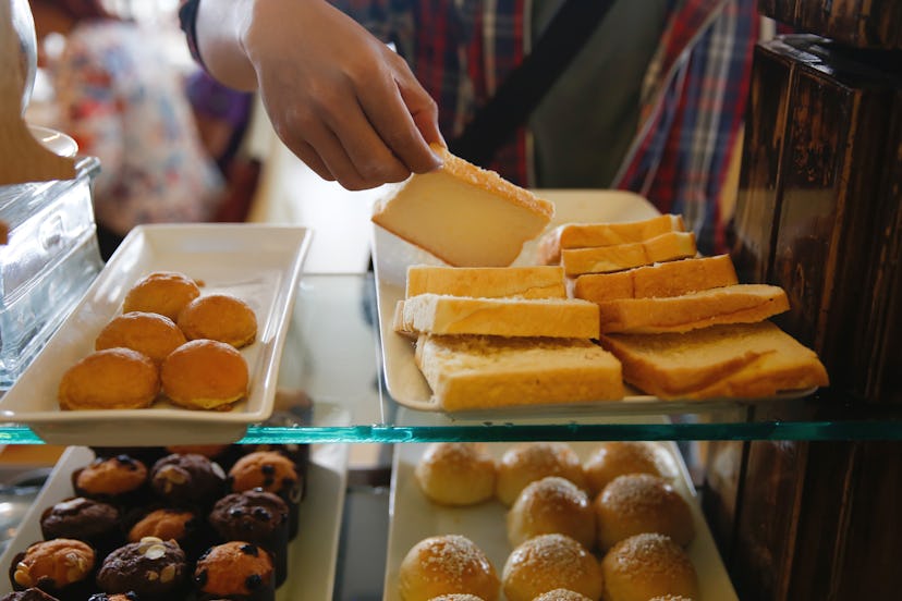 Close-up shot of unrecognizable man taking a slice of bread from breakfast buffet table at hotel res...