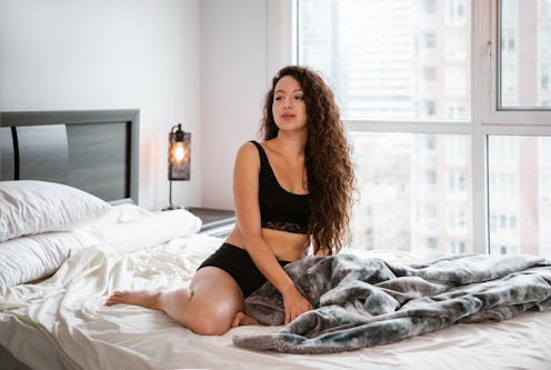 Young mixed race woman waking up in her bedroom. She is dressed in black casual underwear. Interior ...