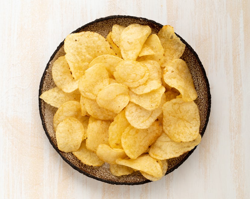 brown yellow chips from natural potato in brown ceramic plate on a white wooden background, top view...