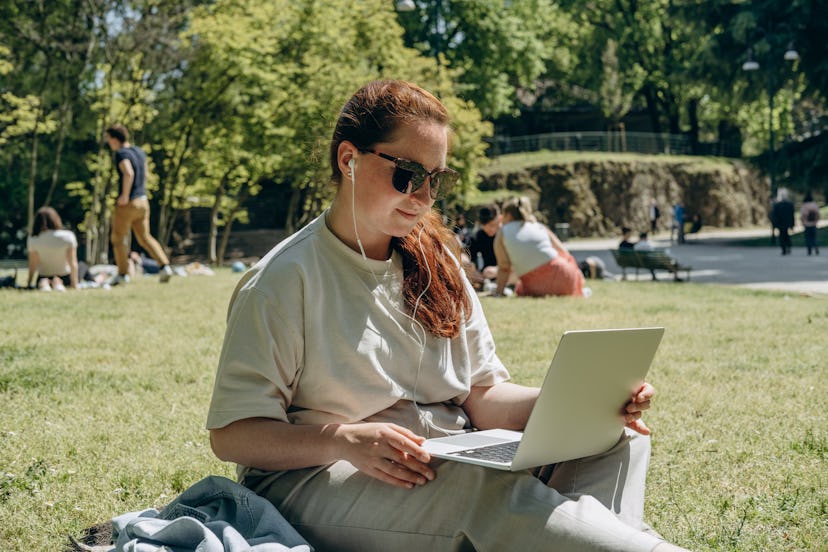 young female student with a laptop studying in the park on the green grass