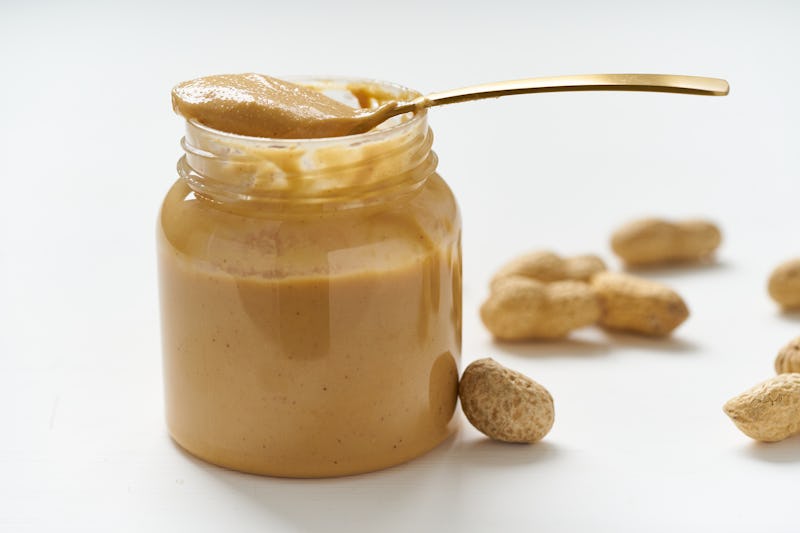 jar of peanut butter and peanuts in a shell on a white table, side view, fresh ground crushed nuts, ...