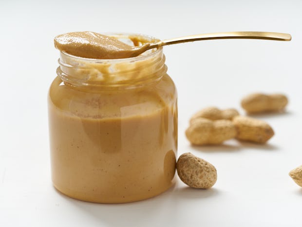 jar of peanut butter and peanuts in a shell on a white table, side view, fresh ground crushed nuts, ...