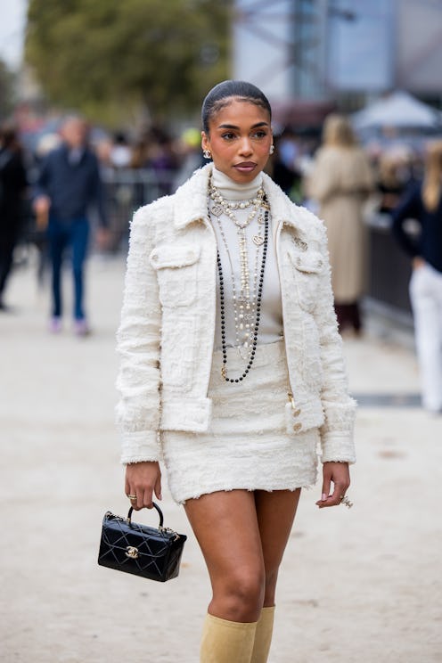 Lori Harvey wears white jacket, skirt, turtleneck, necklace, black bag, beige boots outside Chanel d...