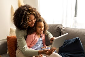 Mother and daughter sitting in the living room and using digital tablet to play the best ipad games ...