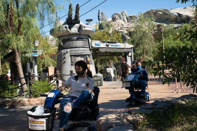Guests wearing protective masks ride scooters past the entrance to the Rise of the Resistance attrac...